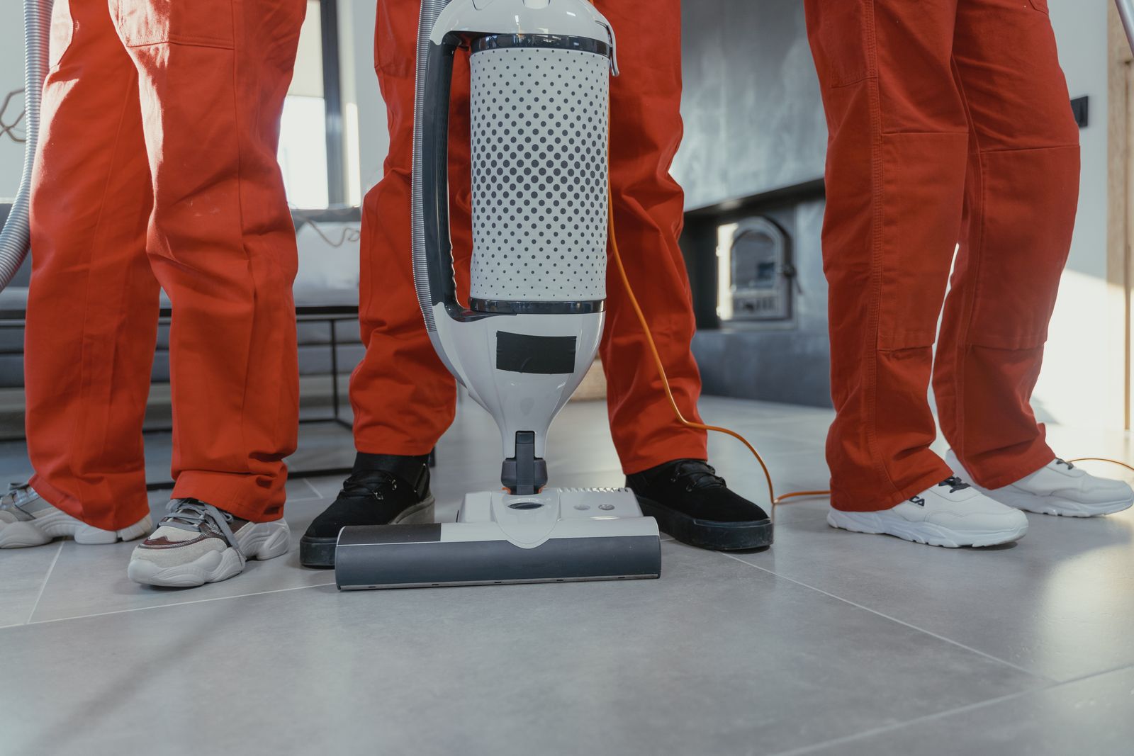 A uniformed cleaning crew with a vacuum standing on a spotless tiled floor in a bright home